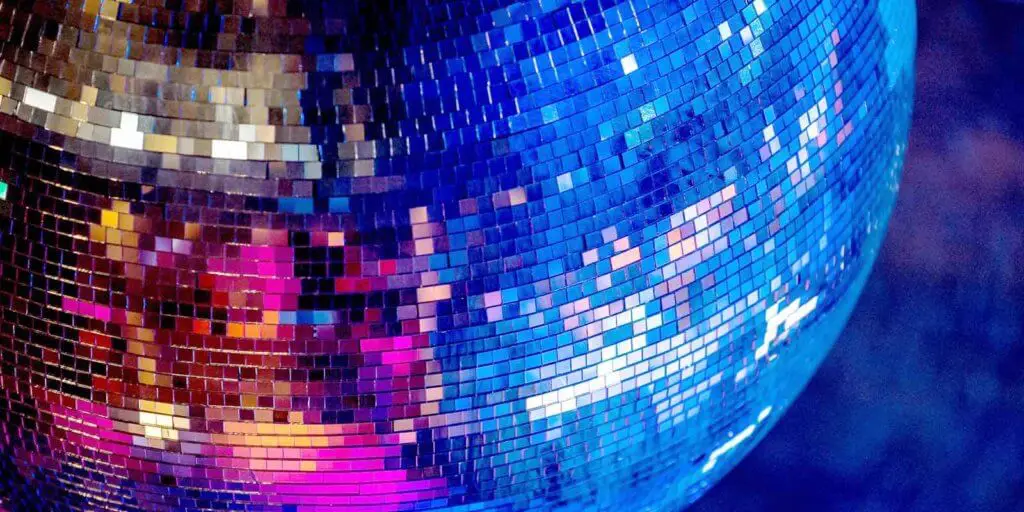 Close up view of a disco ball with blue and bright pink reflecting in the ball.