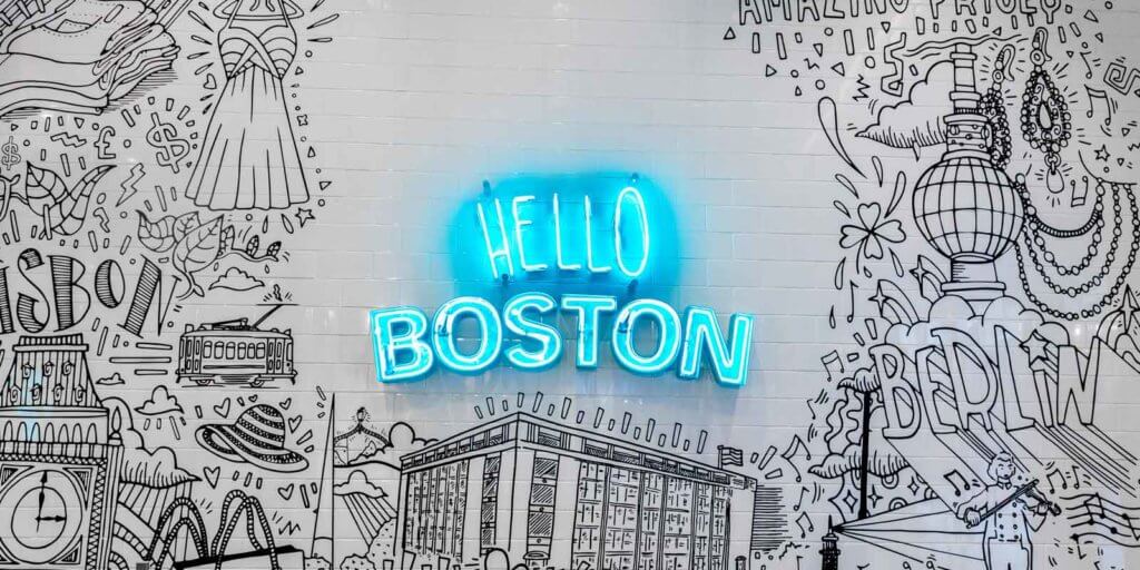 Black and white drawing on subway tile with a blue neon sign in the middle that reads "Hello Boston."