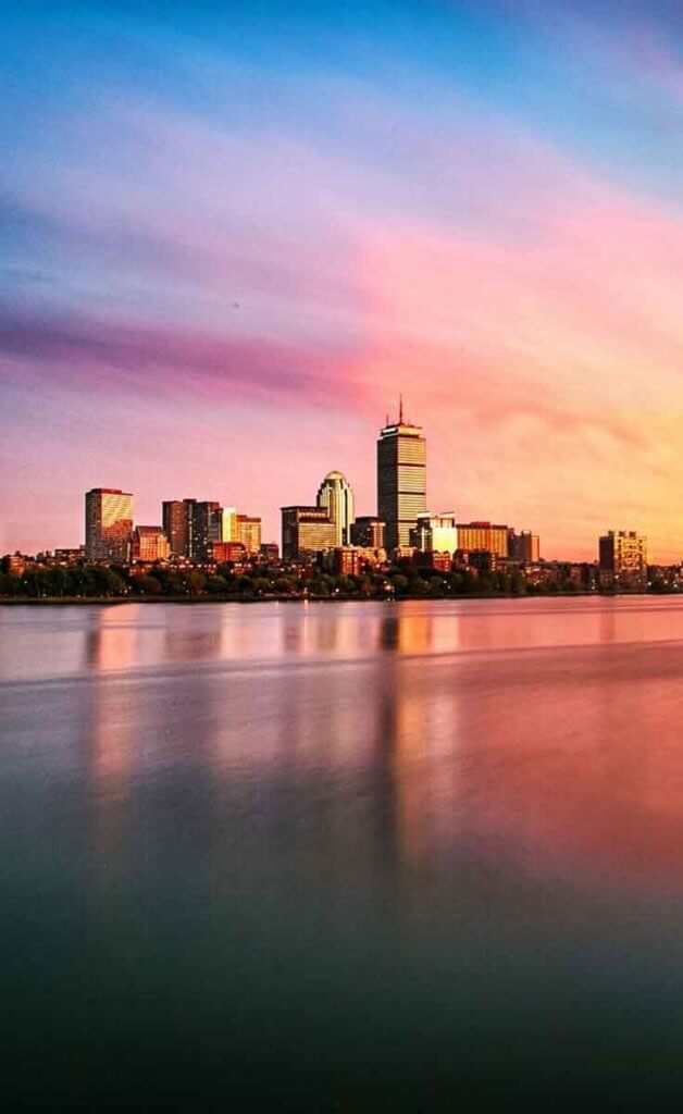 Boston city skyline showing the Prudential Center across the Charles River with cotton candy colored skies during the sunset.
