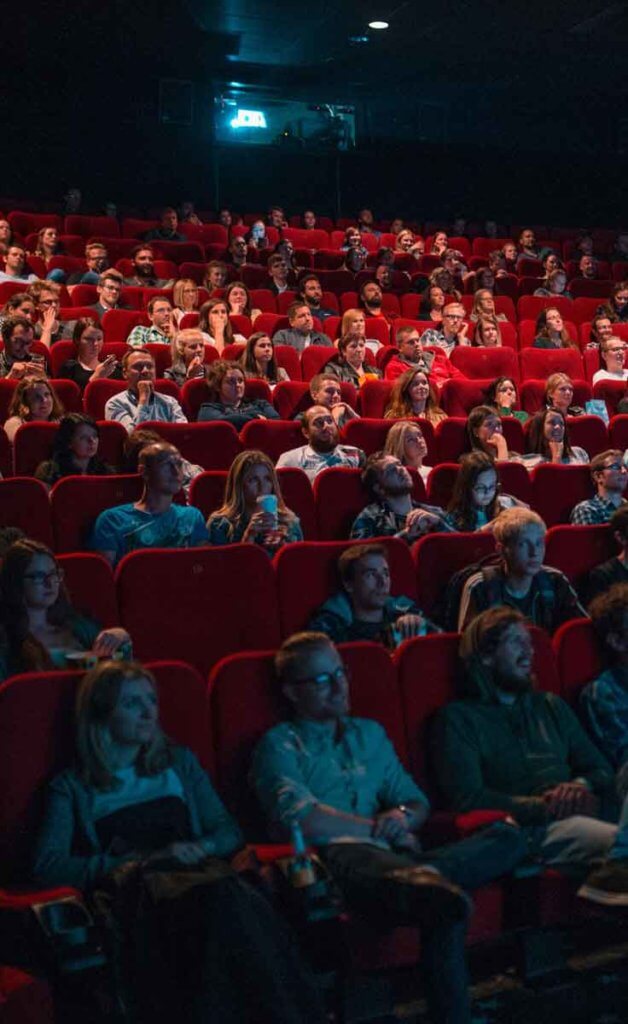 A crowd of people sitting in red seats in a darkened movie theater.