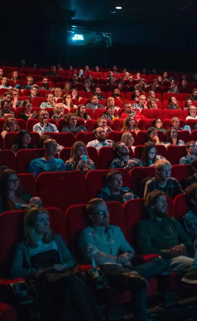 A crowd of people sitting in red seats in a darkened movie theater.
