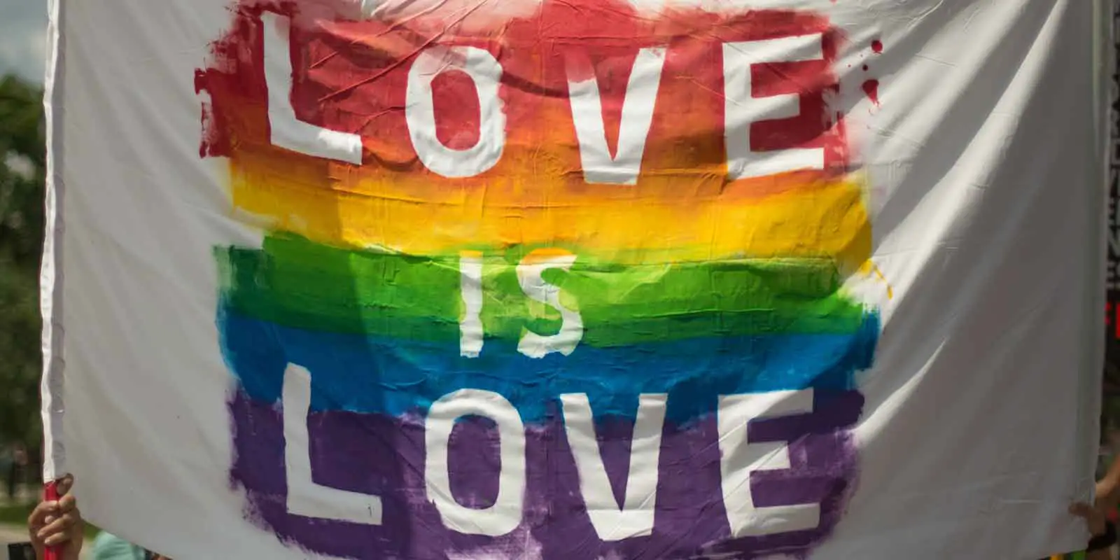 Close up of a sign that says "Love is Love" with rainbow colored stripes behind white letters.