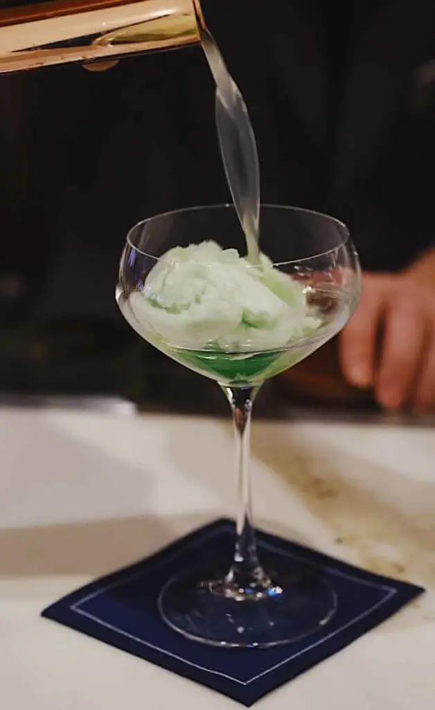 Closeup of a tall stemmed cocktail glass filled with cotton candy with a drink being poured over it.