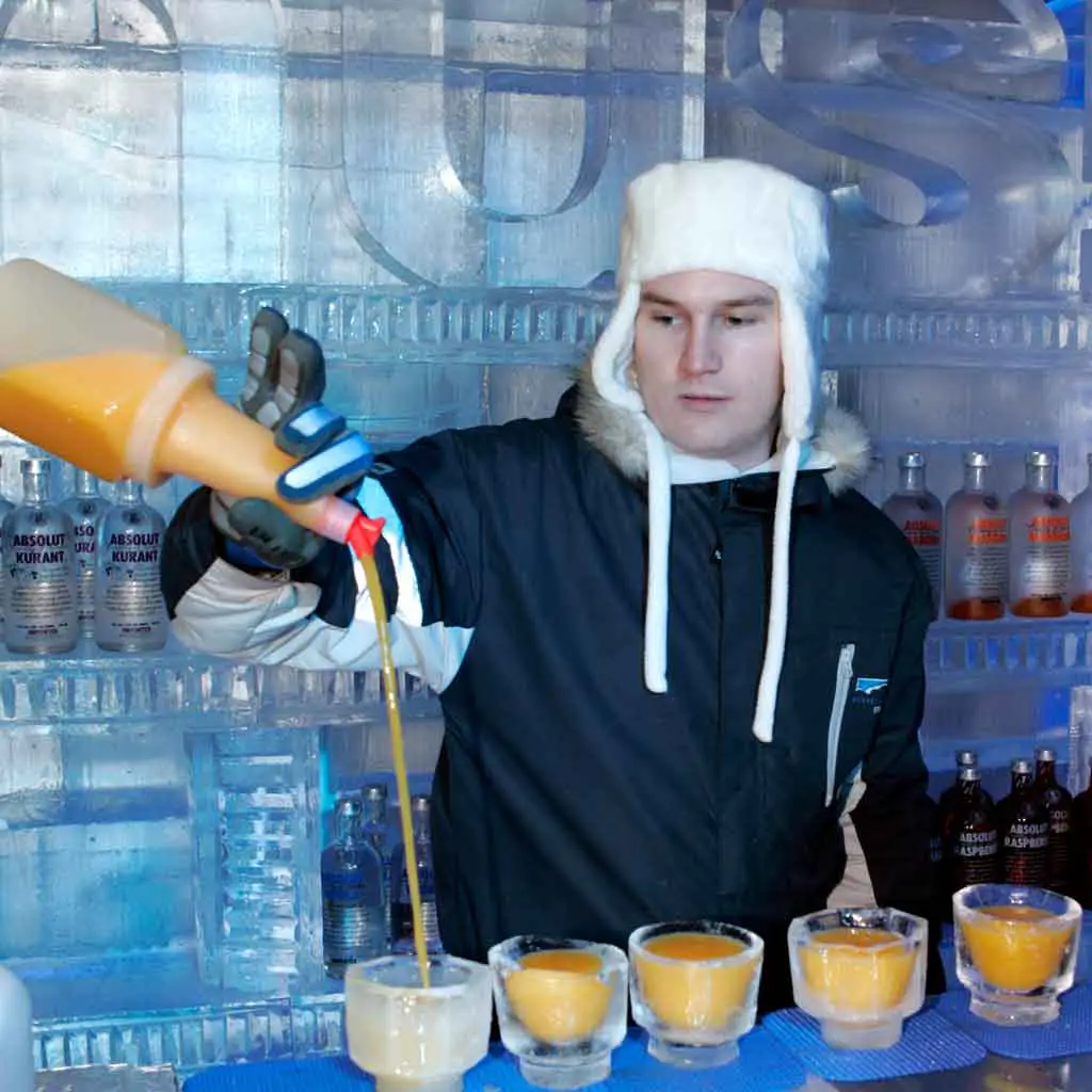 Photograph of a man dressed in Winter gear pouring an orange cocktail at Minus 5 Ice Bar in Las Vegas.