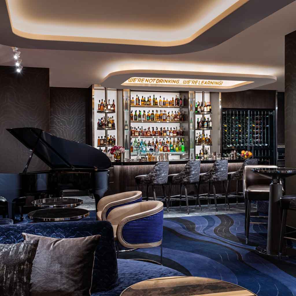 Photograph of Mr. COCO lounge and restaurant, with dark grey and cobalt blue decor, a Steinway piano, and a bar filled with prime liquor. A sign says "We're not drinking...we're learning!"