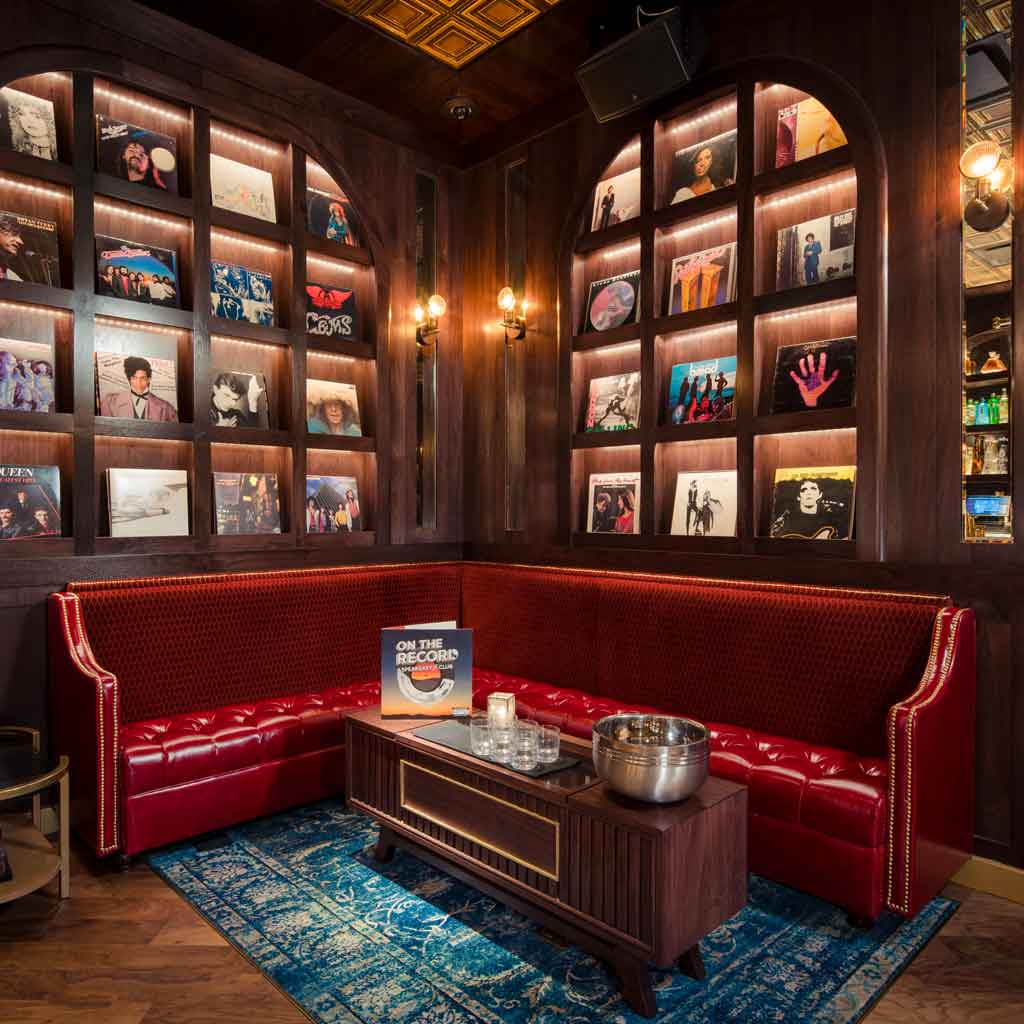 Closeup of a quaint corner at On the Record featuring vintage record albums on shelves and a red leather couch.