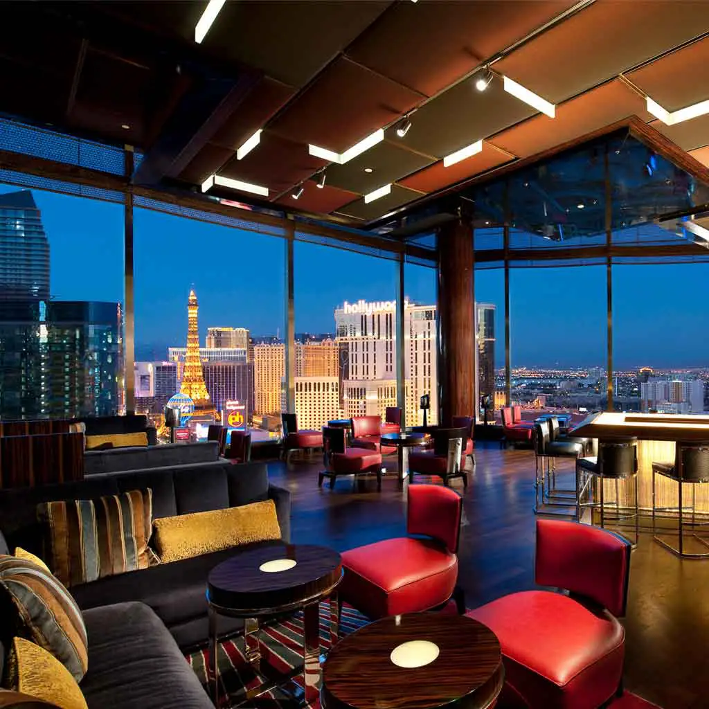 Photograph of an empty SkyBar with the Las Vegas skyline seen through the ceiling to floor windows in the background.