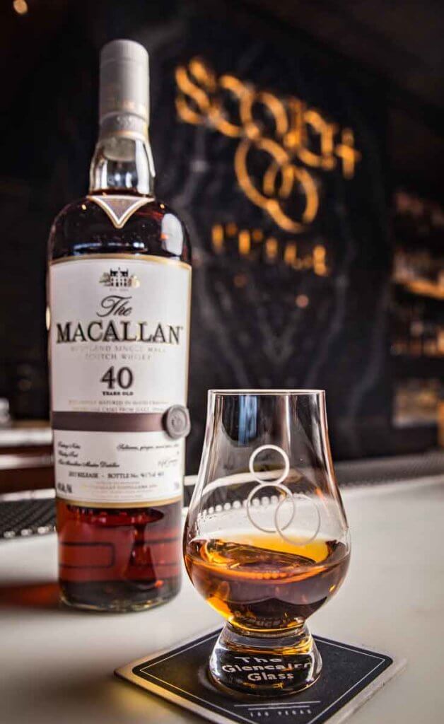Closeup of a bottle of rare Macallan scotch sitting behind a glass of the liquor with the #80 on it.
