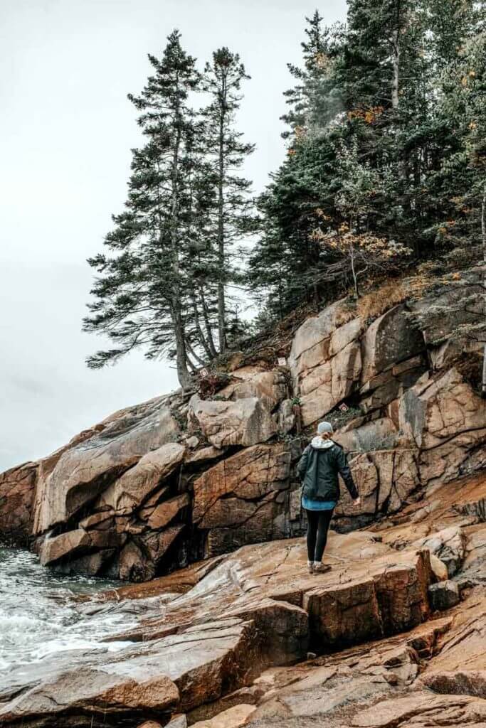 A woman walking up a rocky cliff at Acadia National Park in Maine.