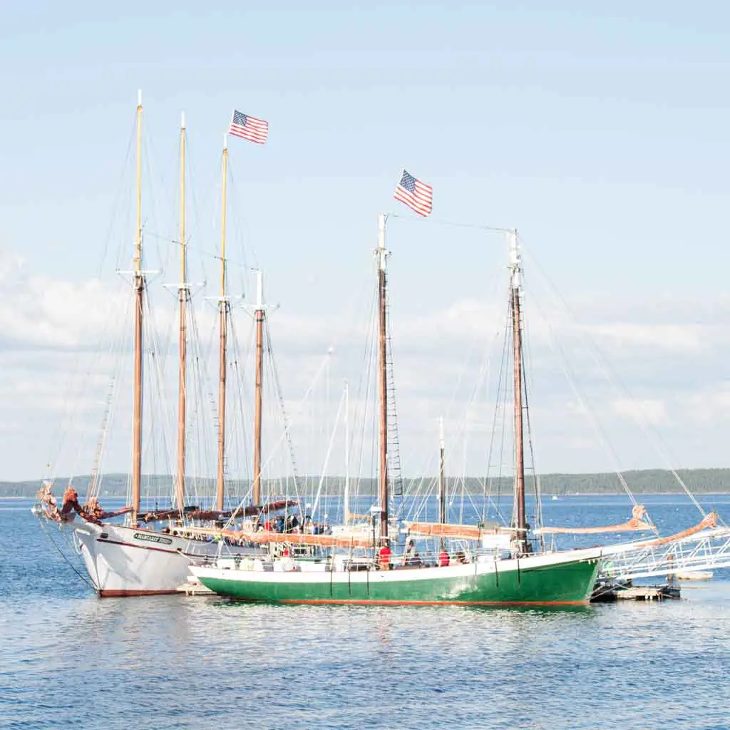 Two sailboats with American flags docked on shore.