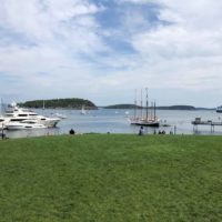 Landscape view of Agamont Park, near the start of the Bar Harbor Shore Path, with a pier, yachts, and sailboats in the distance.