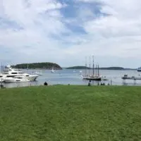 Landscape view of Agamont Park, near the start of the Bar Harbor Shore Path, with a pier, yachts, and sailboats in the distance.