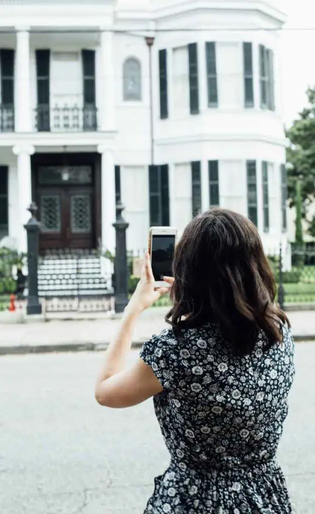 Woman taking a photo of a mansion on a smartphone.