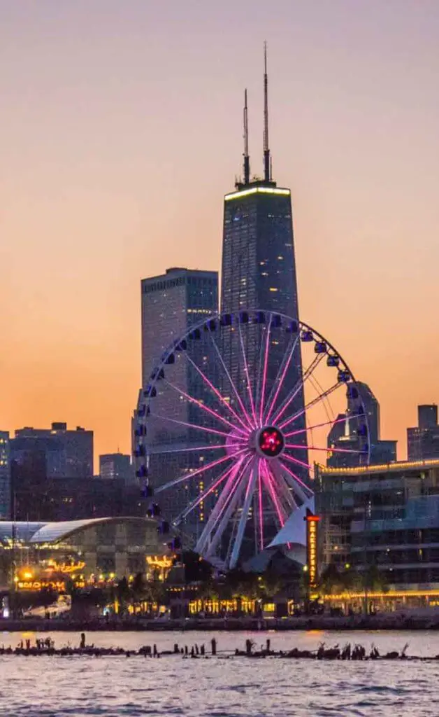 Closeup of the beach along Lake Michigan in Chicago during sunset, with tall buildings and a ferris wheel in the background.