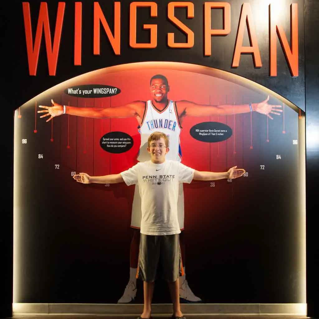 A young boy measures his wingspan against a basketball player at the Naismith Memorial Basketball Hall of Fame in Springfield, MA.