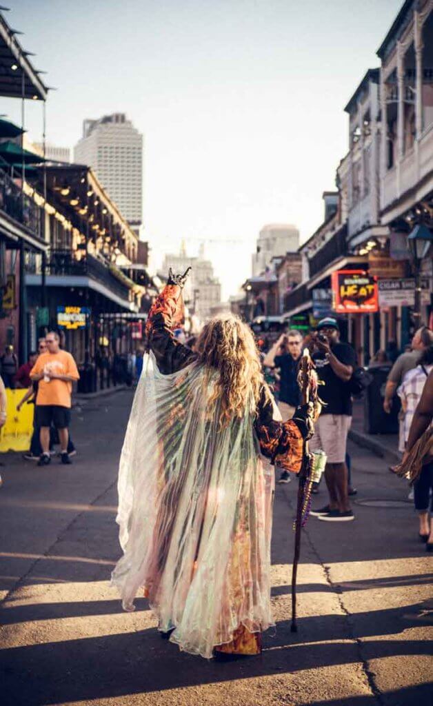 A person dressed in a velvet robe and sheer, irisdescent cape and a staff looking down a crowded street while flashing the 'rock on' hand sign.