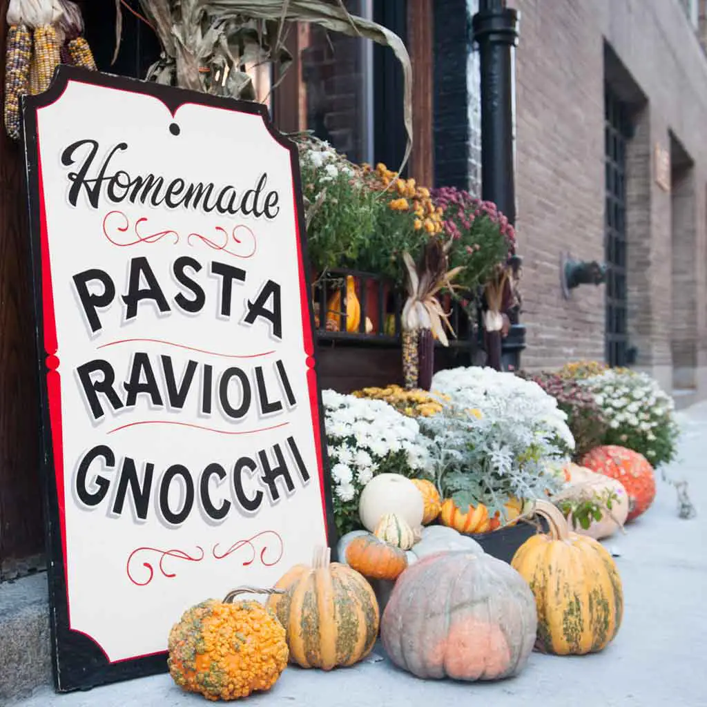 Closeup of a sign that reads "Homemade Pasta Ravioloi Gnocchi" with mums, gourds, and pumpkins surrounding it.