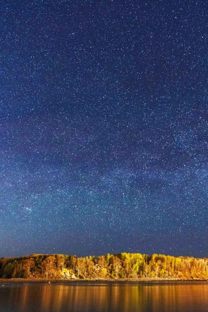 A dark blue sky with countless stars and an island full of trees in the distance.