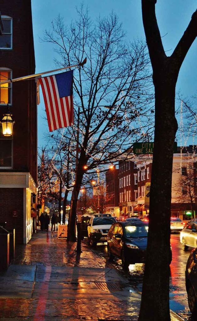 View of Washington Street in Salem, MA during dusk with white lights on bare trees and a American flag hanging from a brick building.