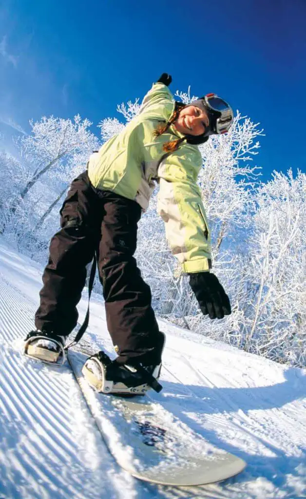 Woman snowboarding down Wachusett Mountain, wearing a light green coat and black ski pants.