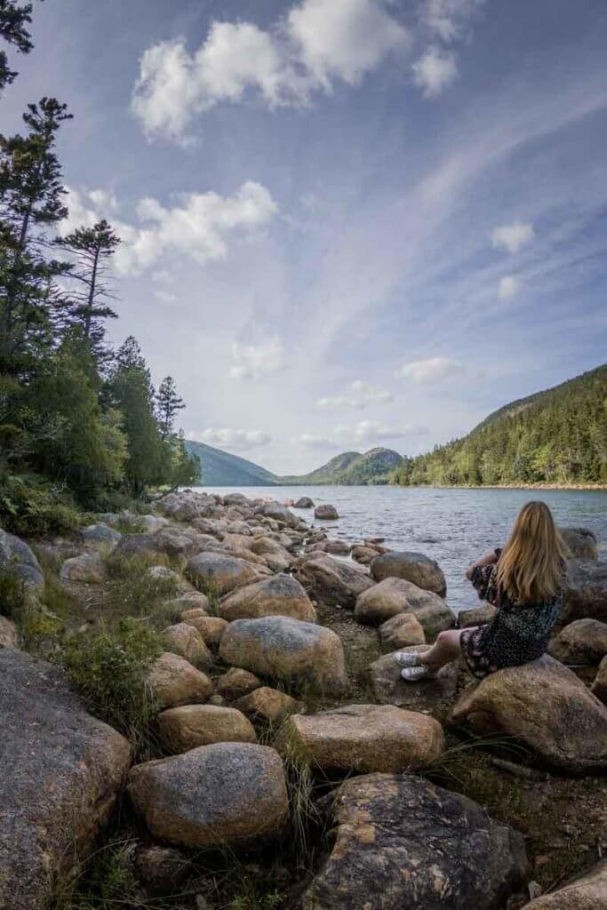 Photo of a woman sitting amidst large rocks along the shoreline of Jordan Pond in Acadia National Park.