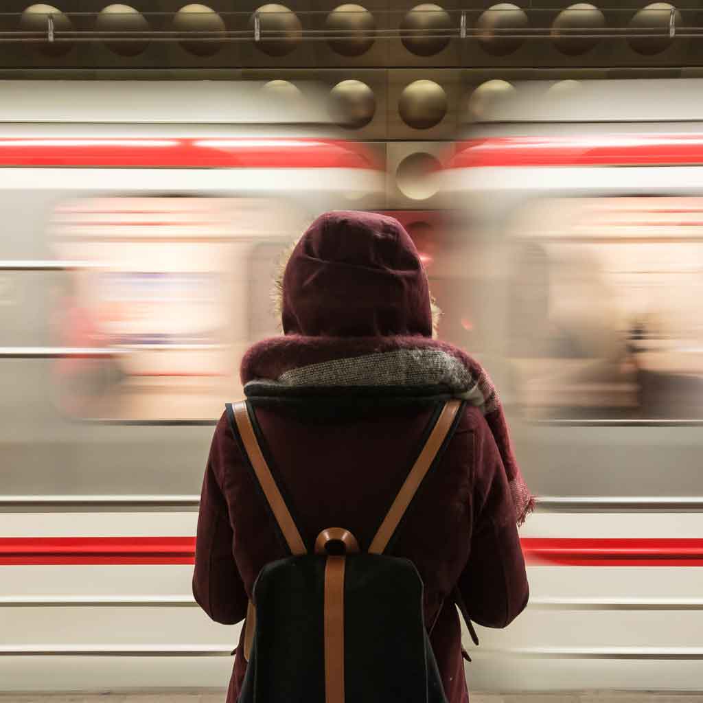 A white and red train speeds by while a woman watches.