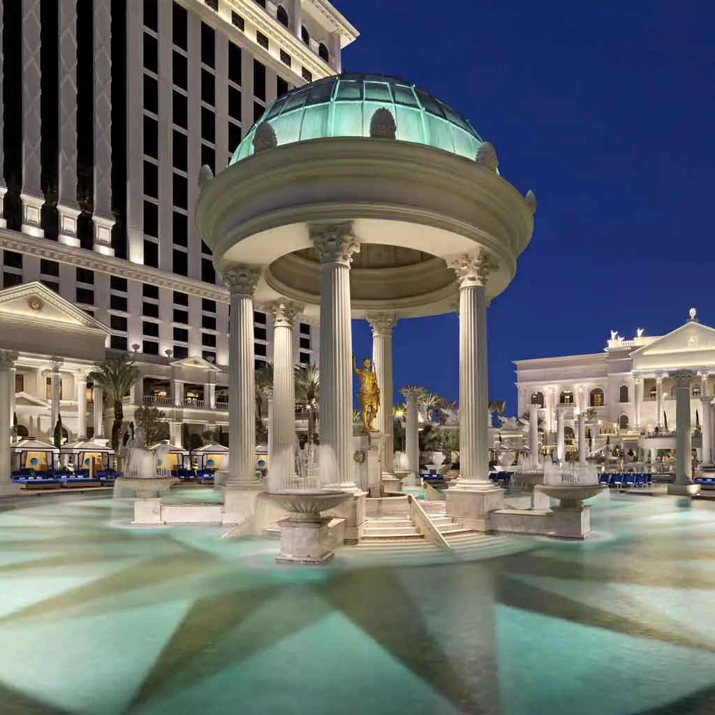 Closeup of a pool with a replica of a Roman temple in the middle with a hotel in the background.