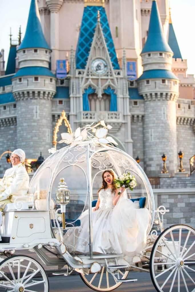 Bride sitting in a pumpkin shaped coach in front of a castle.