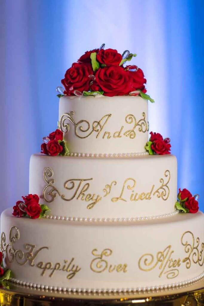 Closeup of a white and gold wedding cake covered in red roses. Text on the cake reads "And they lived happily ever after."