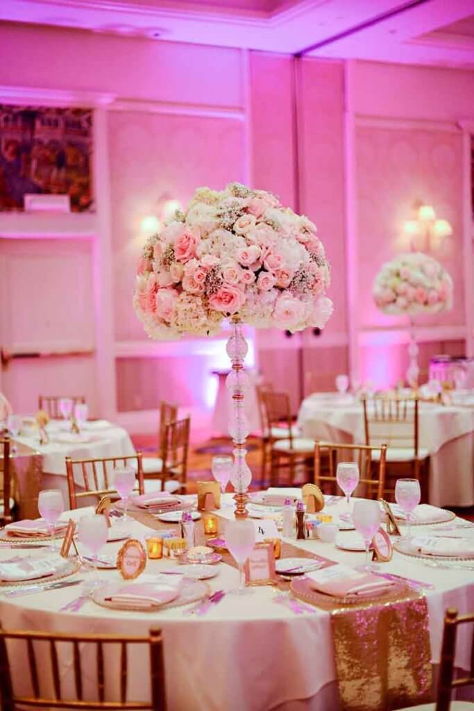 Photo of a table with a fancy setting for a wedding with a tall crystal vase filled with white and pink flowers.