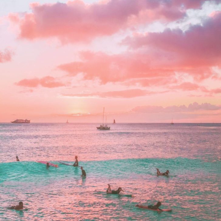 Photo of people waiting in the surf for a good wave with boats in the background.