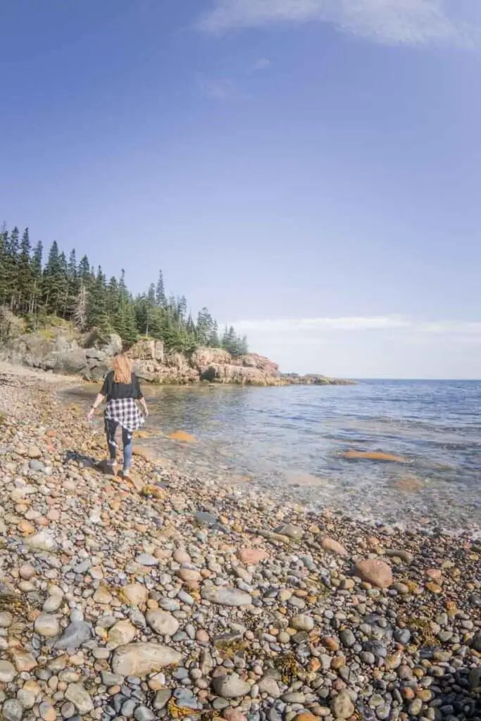 Woman walking across the rocky coastline at Little Hunters Beach in Acadia National Park.