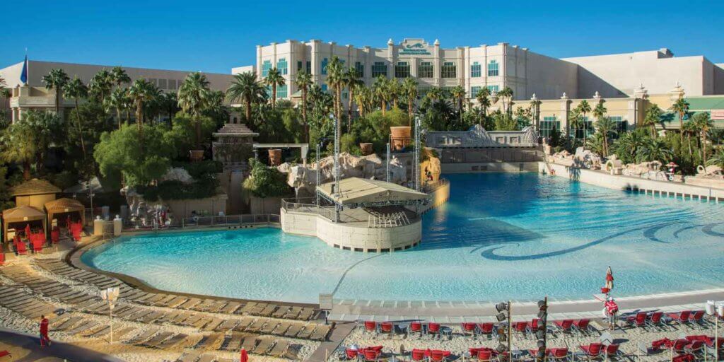 Landscape view of a pool with a sand beach and a hotel in the background.