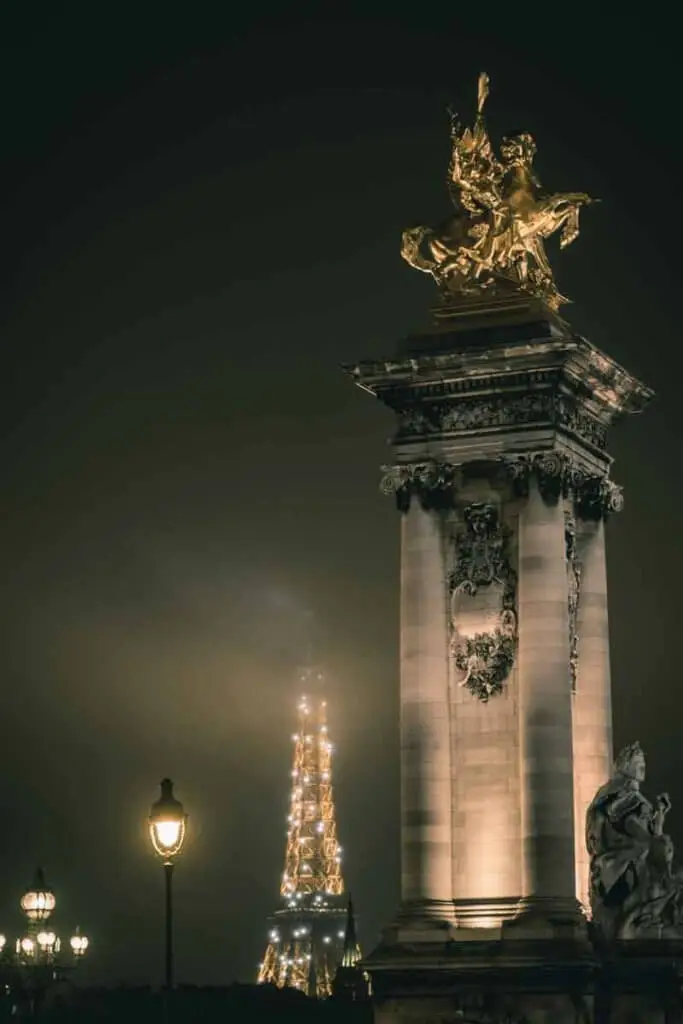 Nighttime photo of a a statue in Paris, France with the Eiffel Tower in the background and lots of fog.