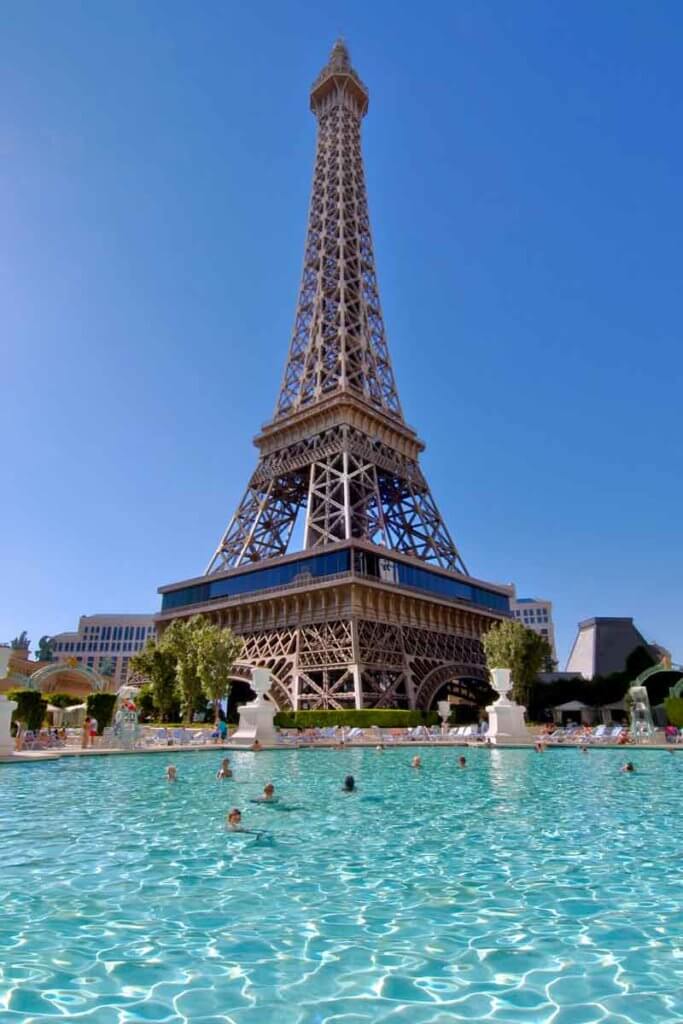 A pool with people in it beneath a replica of the Eiffel Tower.