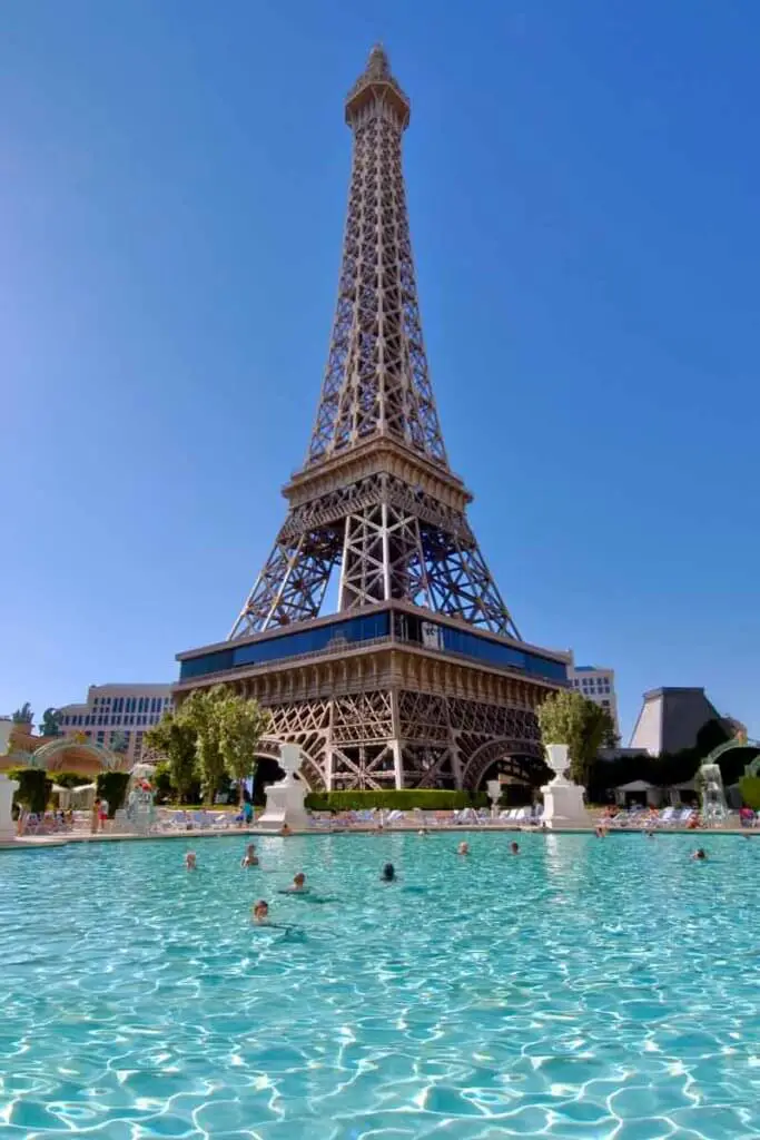A pool with people in it beneath a replica of the Eiffel Tower.