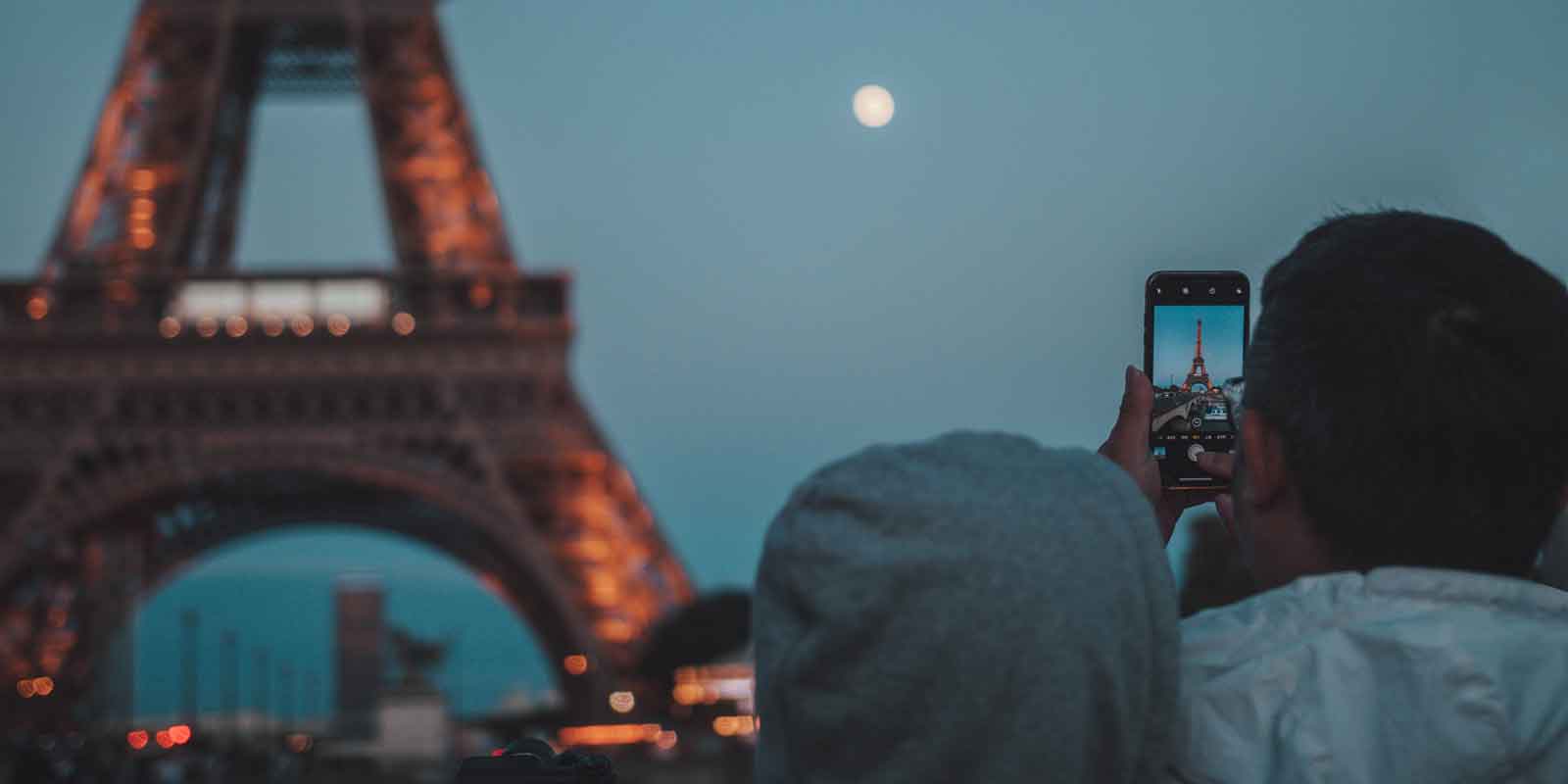 Photo of a man taking a photo of the Eiffel Tower with a smartphone camera.