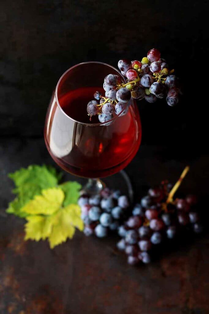 Closeup of a glass of red wine with several bunches of grapes.