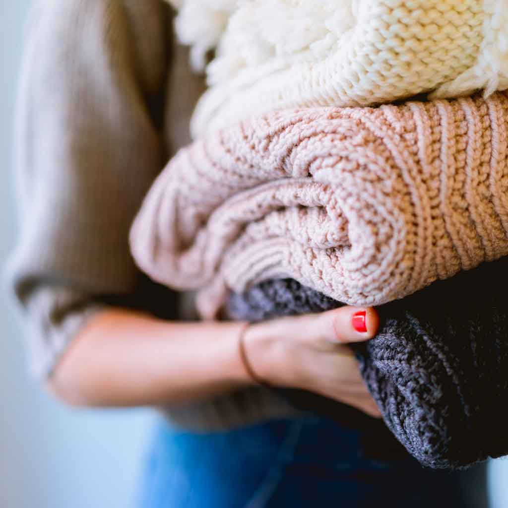 Closeup of a person holding a pile of folded sweaters.