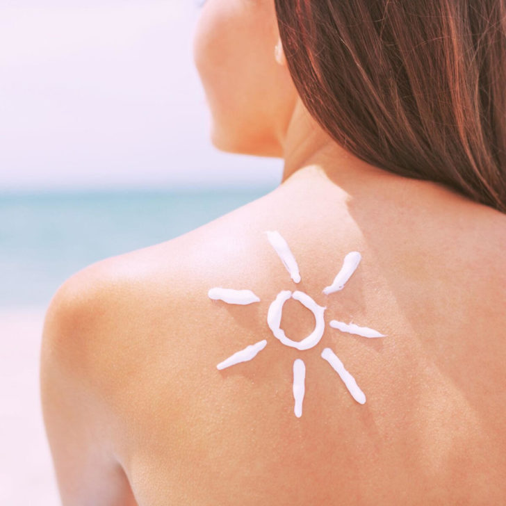 Photo of a woman from behind with sunscreen applied in the shape of the sun on her shoulder.