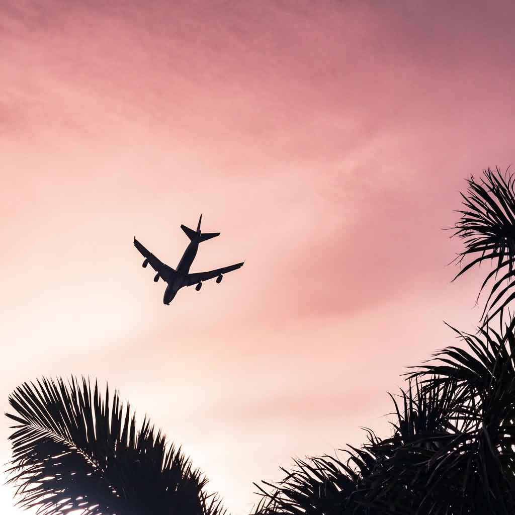 Silhouette of a plane flying through a pink sky.