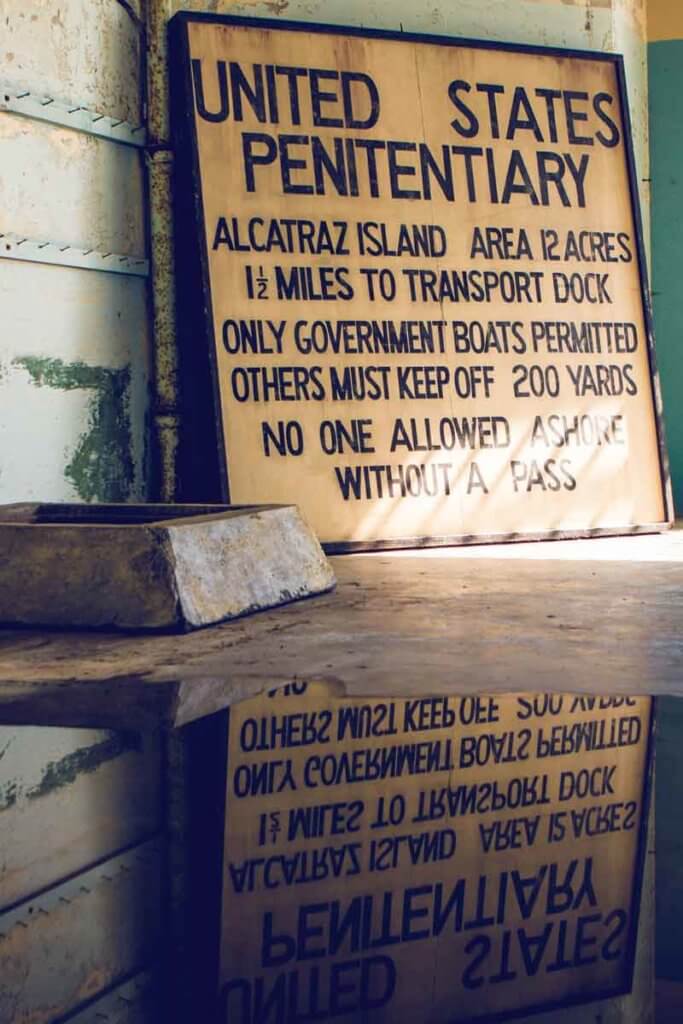 Closeup photo of a sign that says "United States Penitentiary. Alcatraz Island. Area 12 acres. 1.5 miles to transport dock. Only government boats permitted. Others must keep off 200 yards. No one allowed ashore without a pass."