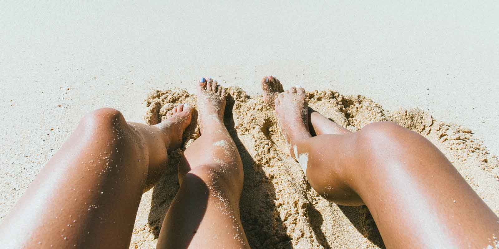 Two tanned legs outstretched on sand.