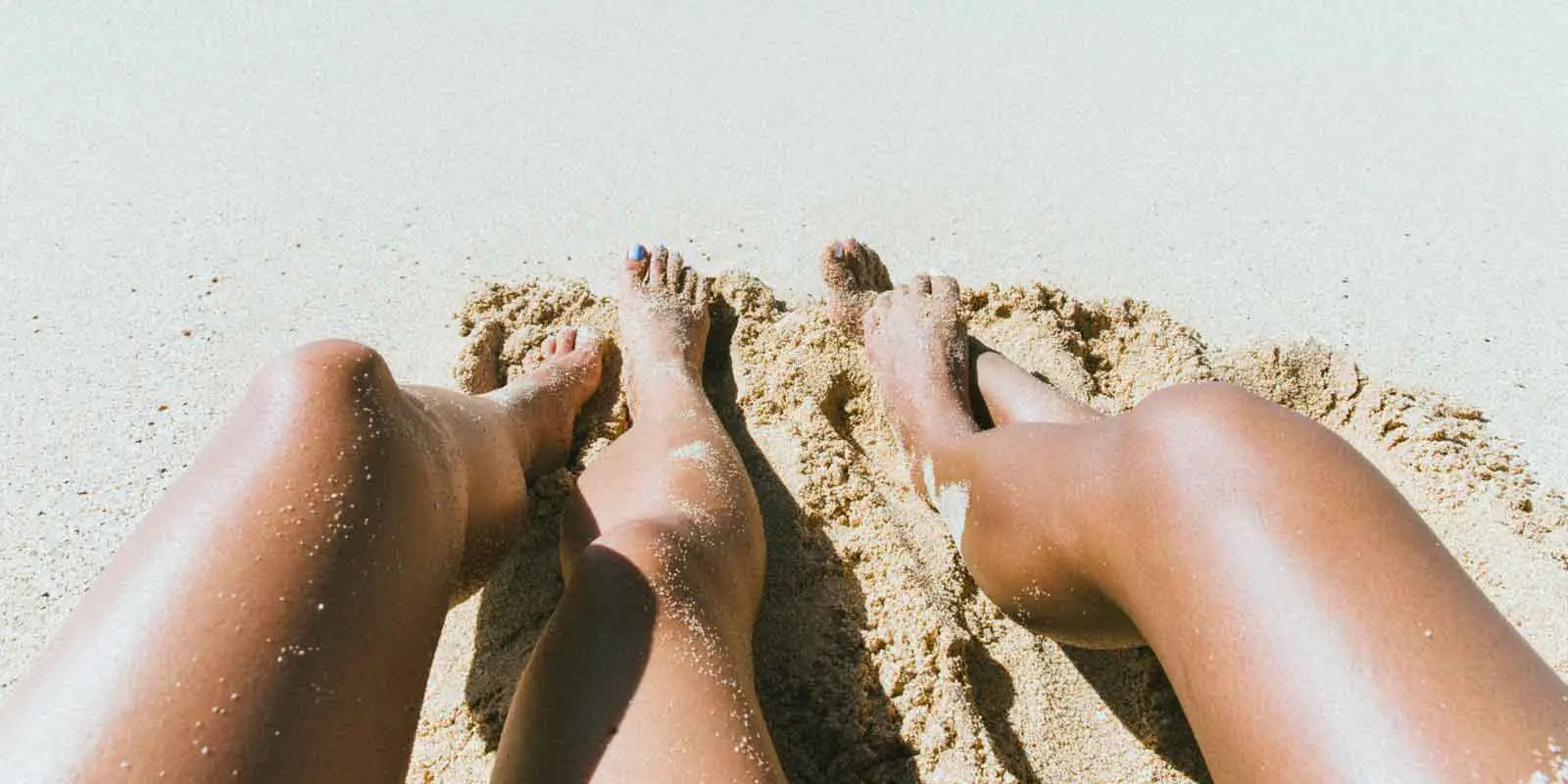 Two tanned legs outstretched on sand.
