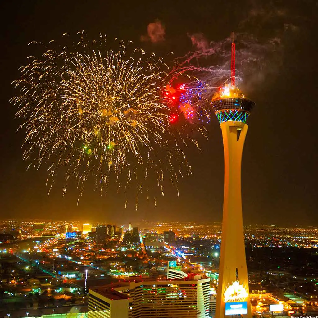 A tall observatory tower set against a city skyline with fireworks bursting.