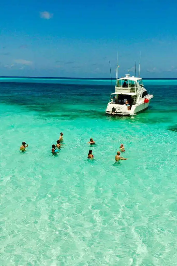 People standing in a turquoise ocean with a boat nearby.