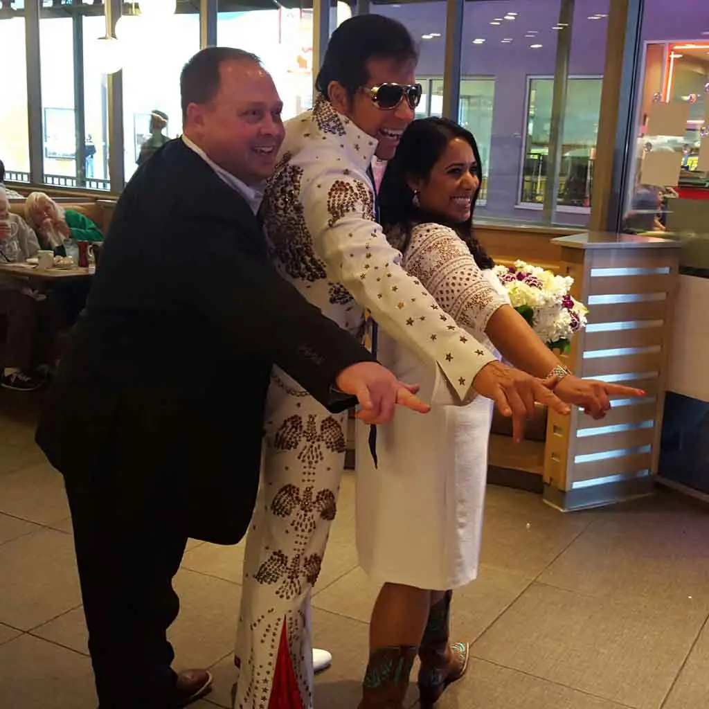 Photo of a bride and groom with an Elvis Presley impersonator in the middle.