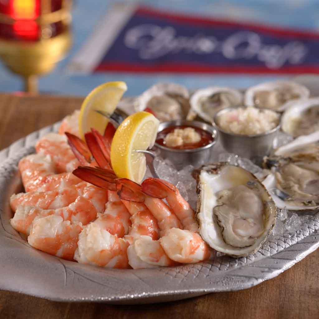 Closeup of a plate of oysters and shrimp cocktail on ice.