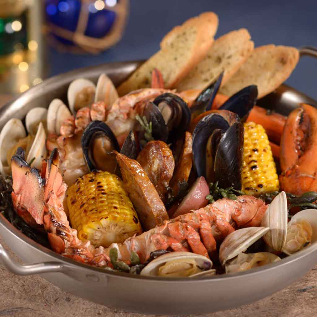 Closeup of a seafood boil plate with lobster, mussels, corn on the cob, and more.