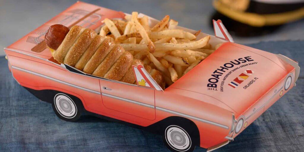Closeup photo of a hot dog wrapped in a croissant and french fries nestled in a cardboard container shaped like a pink convertible.